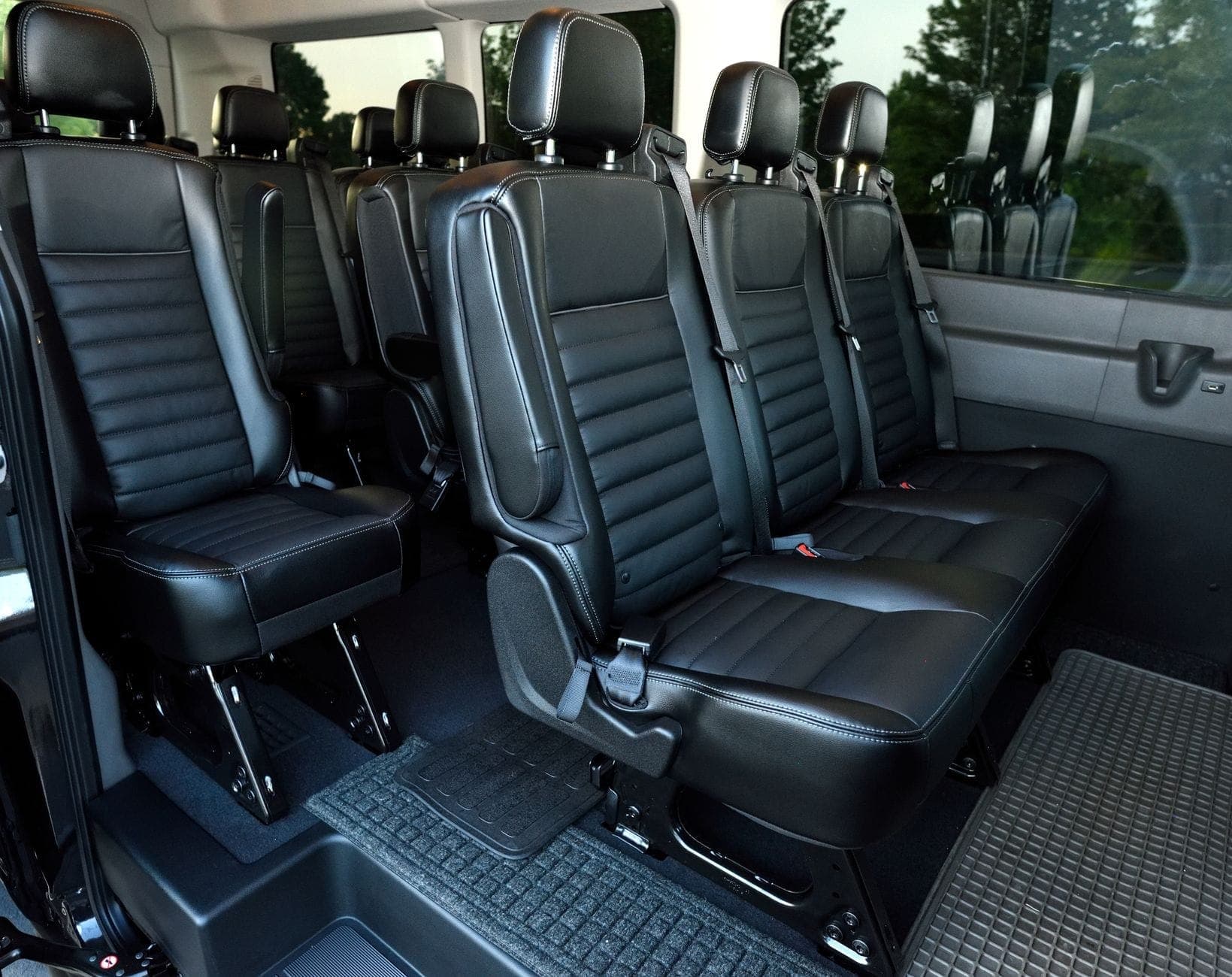 Inside a maxi cab: rows of black leather passenger seats with full-height headrests, three-point seatbelts and standing legroom between rows