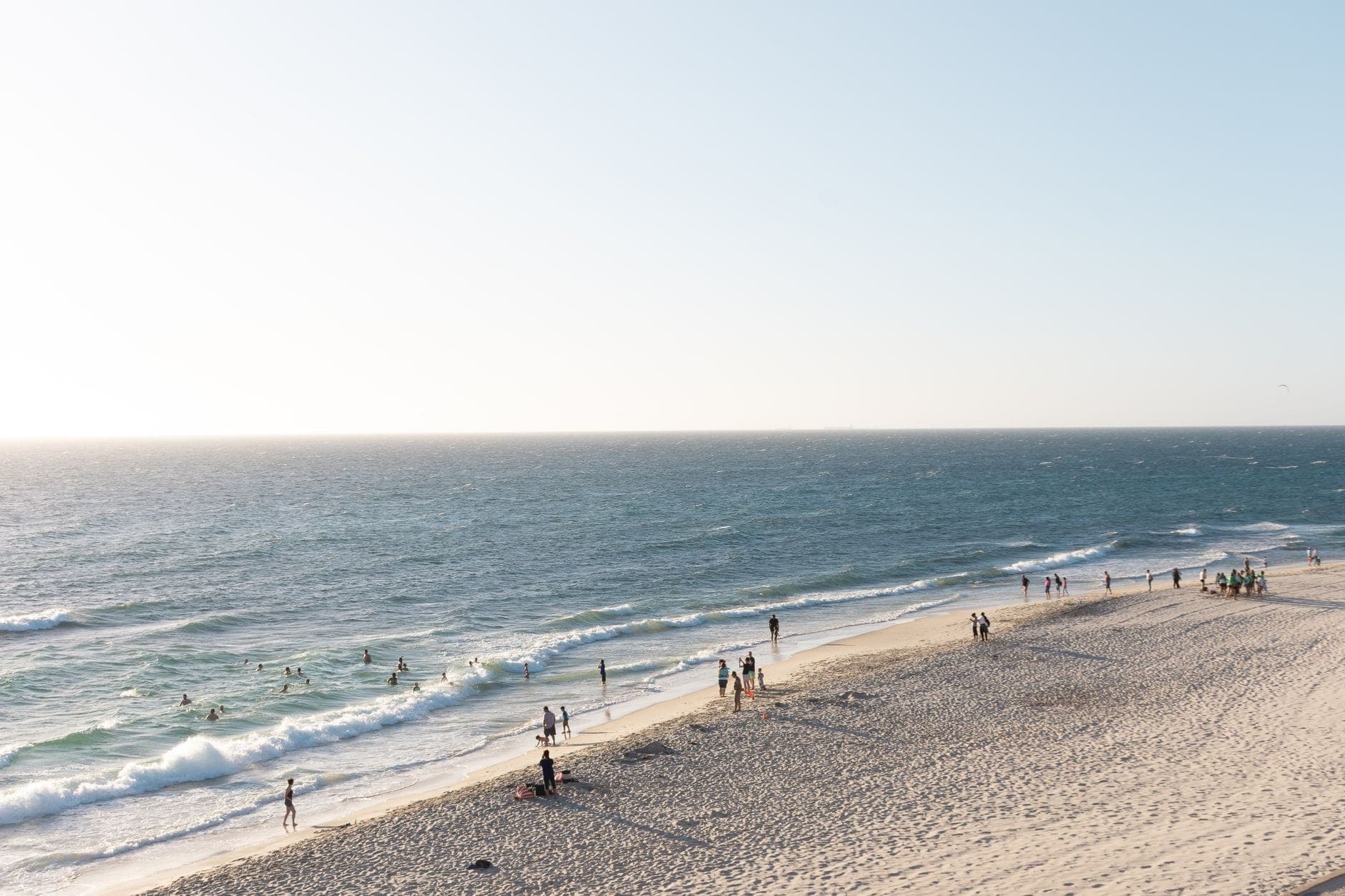 Aerial view of Cottesloe Beach in Perth with swimmers and breaking surf, a western-suburbs maxi cab destination. Maxi Cab Perth runs fixed-fare maxi taxi pickups in Hillarys.
