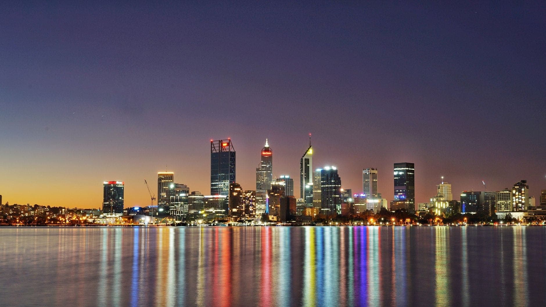 Perth city skyline at twilight reflected in the water, when late-night maxi cab bookings peak. Maxi Cab Perth runs fixed-fare maxi taxi pickups in Northbridge.